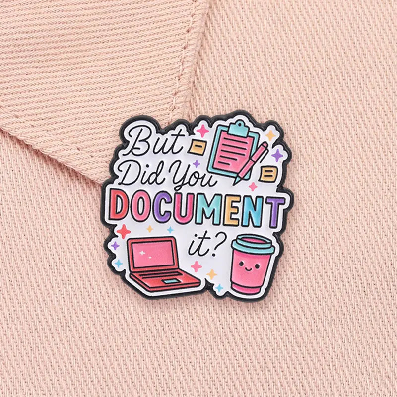 An enamel pin featuring text 'But Did You Document It?' surrounded by icons of a laptop and a drink on a pink fabric backgrou