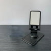 A black desktop stand for a phone or tablet with a rotating adjustable mount.