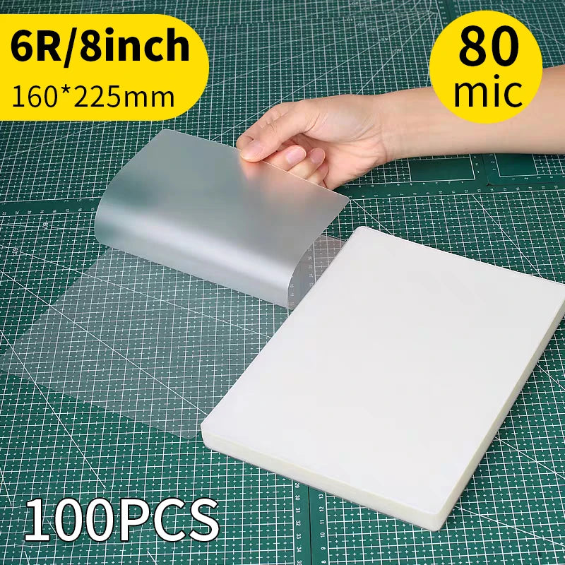A hand holds a silver thermal laminating pouch, measuring 6R/8inch (160x225mm), on a green cutting mat.