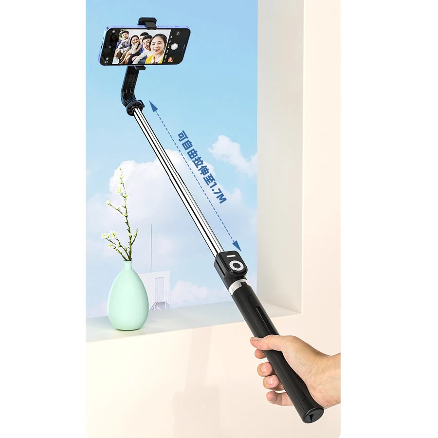 A hand holds an extendable phone tripod with an LED ring light and mirror, demonstrating its reach.