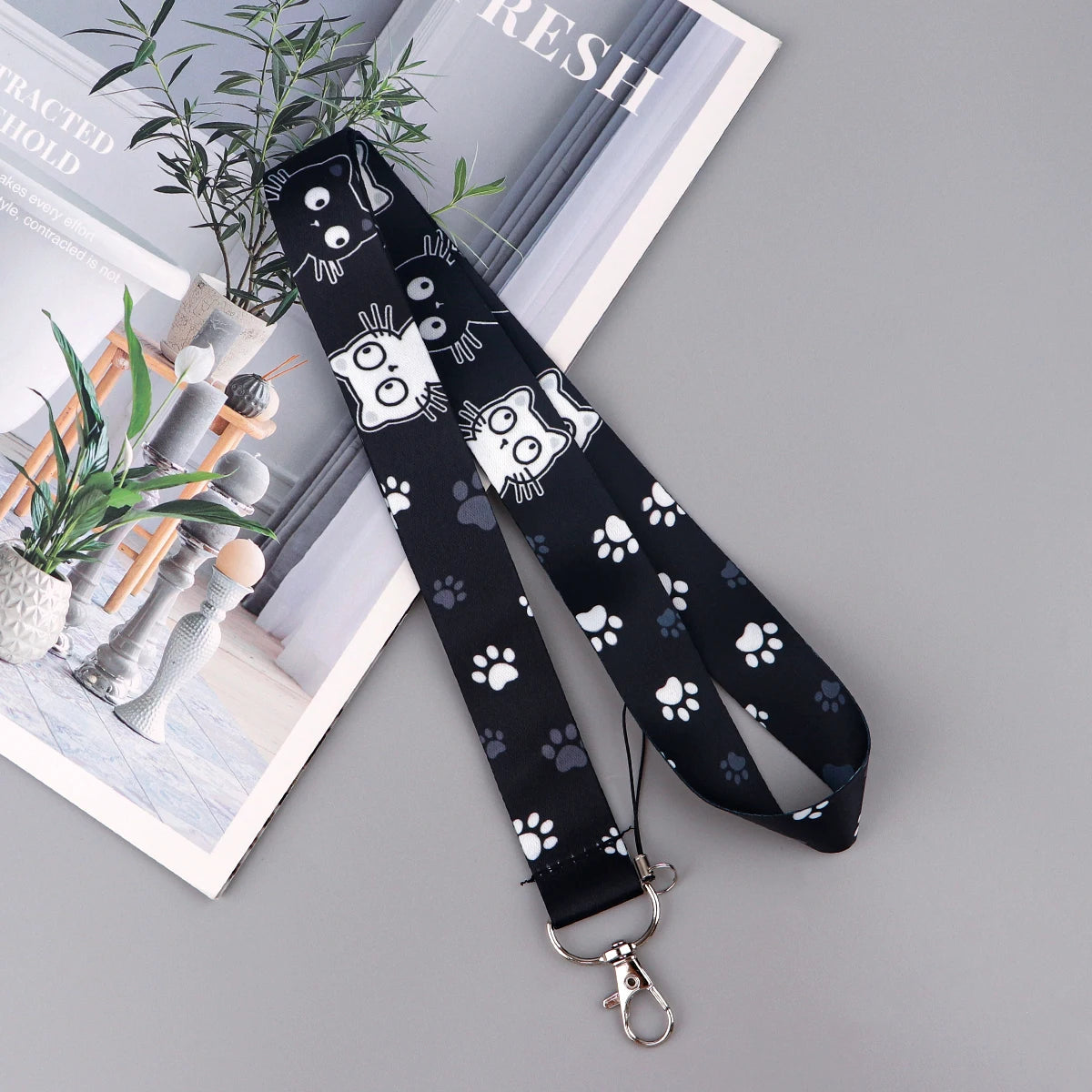 Black lanyard with a cartoon cat design and paw print pattern displayed on a white background.