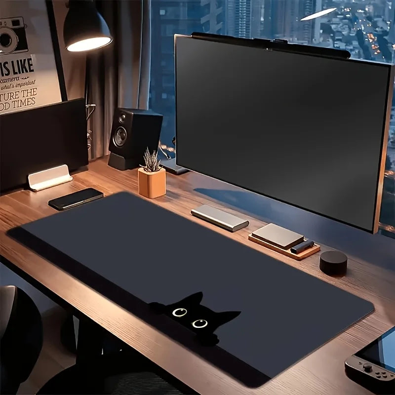 A large dark gray cat silhouette mouse pad is displayed on a wooden desk next to a monitor and speakers.