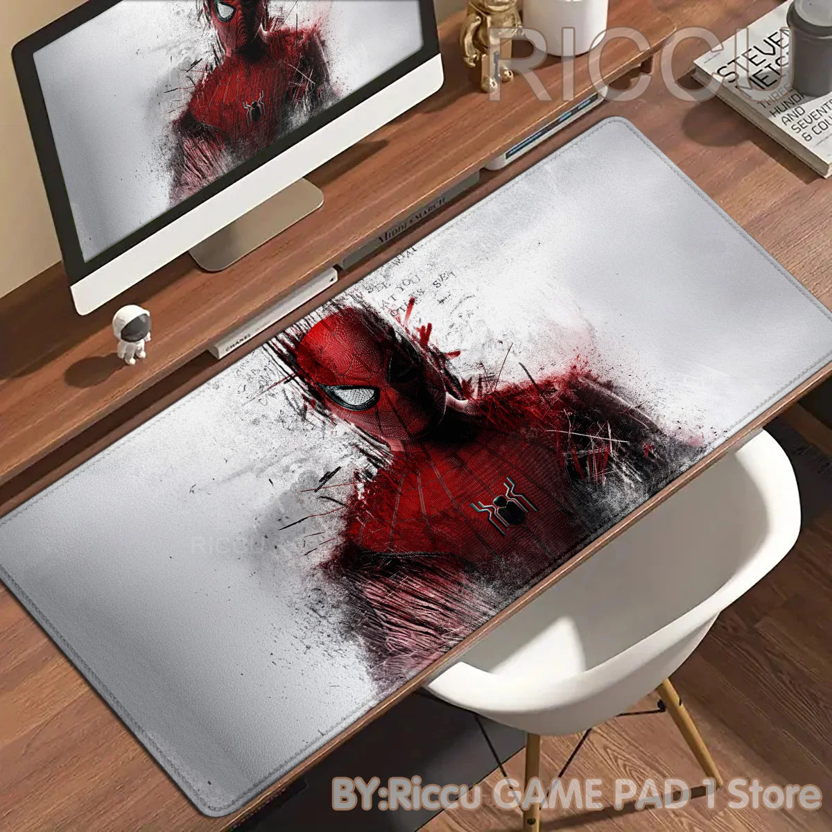 A red and black Spider-Man themed desk mat featuring an anime design placed on a wooden desk next to a computer monitor.