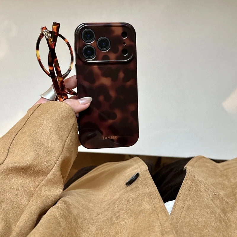 A hand holds a brown leopard print phone case for an iPhone next to a pair of sunglasses.