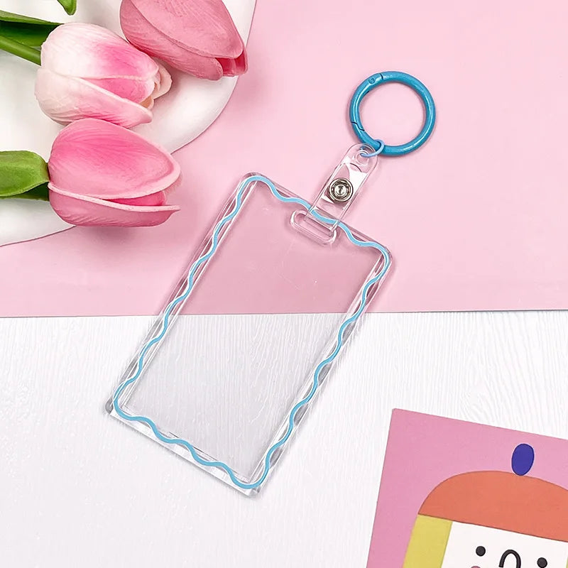 Clear acrylic card holder with a blue keychain attached, displayed on a pink background.