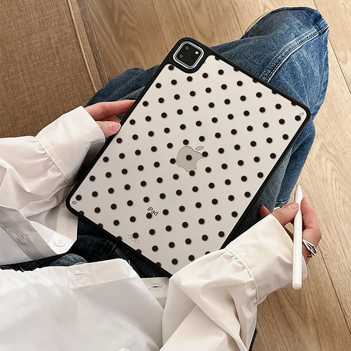 A hand holds a black polka dot protective case for an iPad Pro against a wooden background.