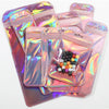 A stack of iridescent pink and purple self-sealing jewelry pouches with resealable zip locks containing a set of dice.