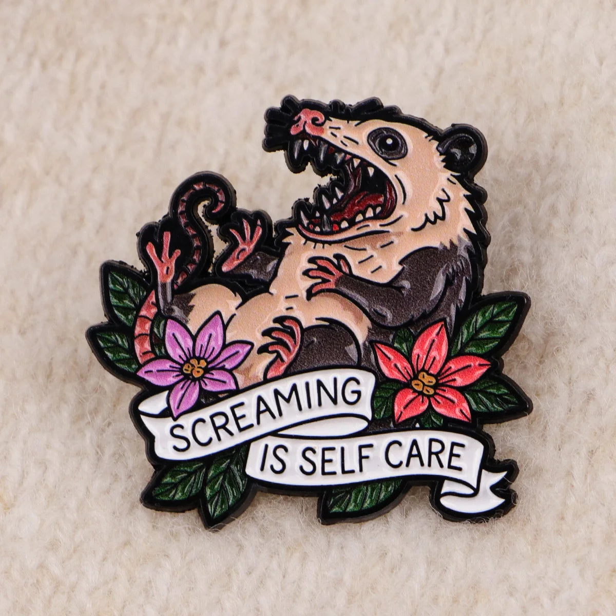 Broche émail représentant un visage de raton laveur féroce avec une expression grondante, entouré de fleurs roses et rouges e