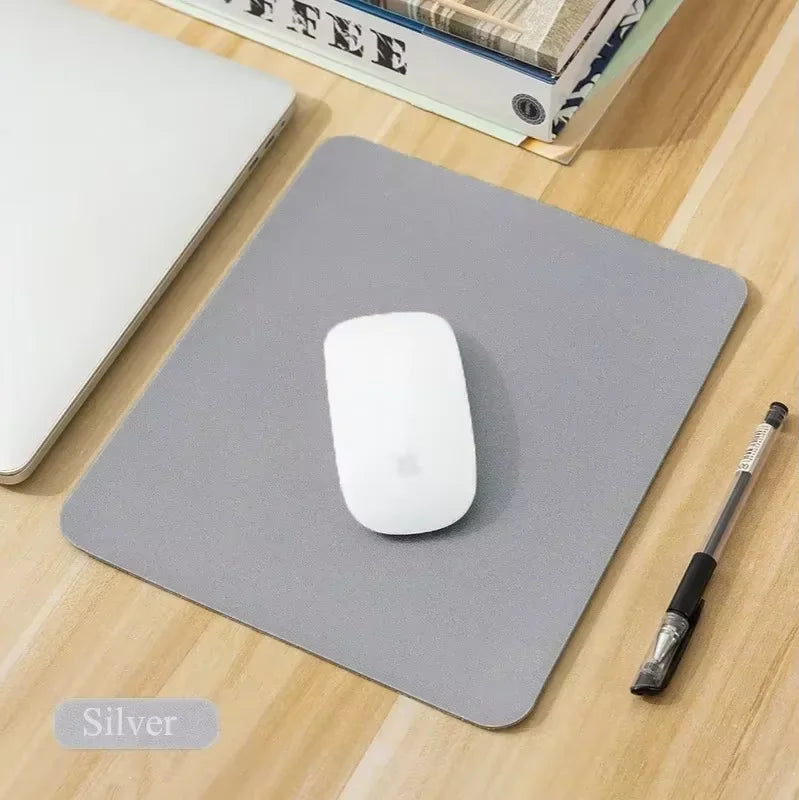 A silver portable gaming mouse pad with a white mouse and a black stylus are displayed on a wooden surface.
