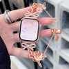 A hand holds a pink smartwatch with a rose gold butterfly watch strap and matching accessories.
