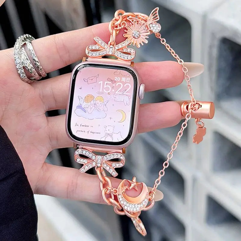 A hand holds a pink smartwatch with a rose gold butterfly watch strap and matching accessories.