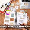 A close-up of a spiral notebook filled with various documents and jumbo acrylic paper clips on a wooden desk.