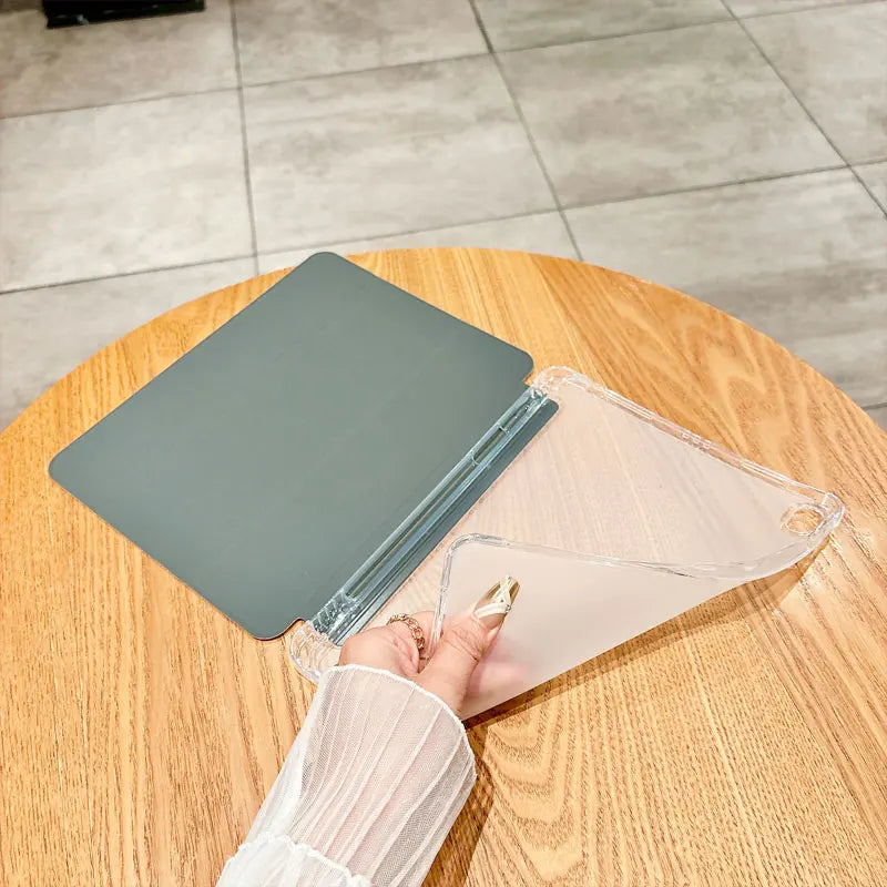 A hand holds a clear anti-drop tablet case for an iPad on a wooden table.
