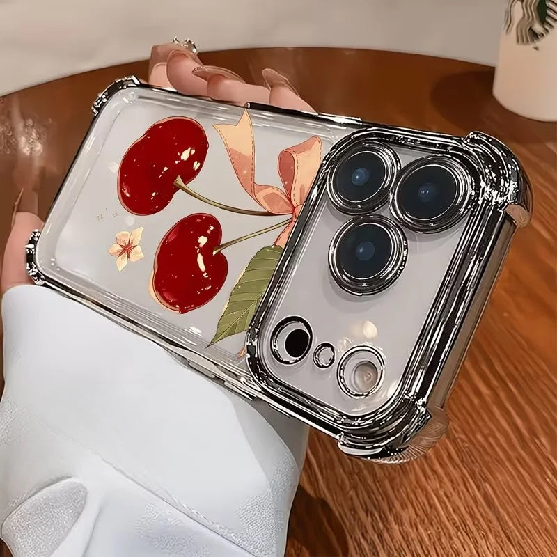 A clear iPhone case with a cherry bow pattern and electroplated finish is held by a person on a wooden surface.