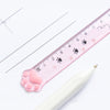 A pink plastic ruler marked with cat paw prints is shown next to a white pen.