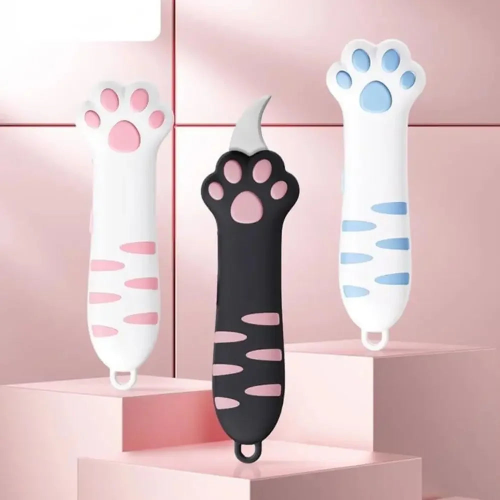 White and black cat paw-shaped box cutter with titanium steel blade displayed on pink tiered stands