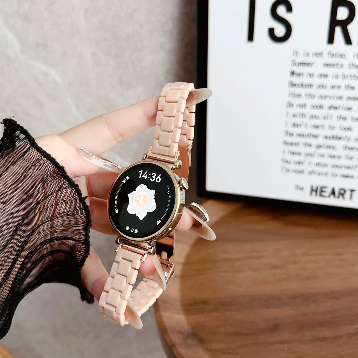 A close-up shot of a light pink resin beaded watch with a black face and gold accents, worn on a hand.