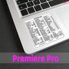 A close-up of a laptop keyboard displaying the Premiere Pro shortcut quick reference sticker.