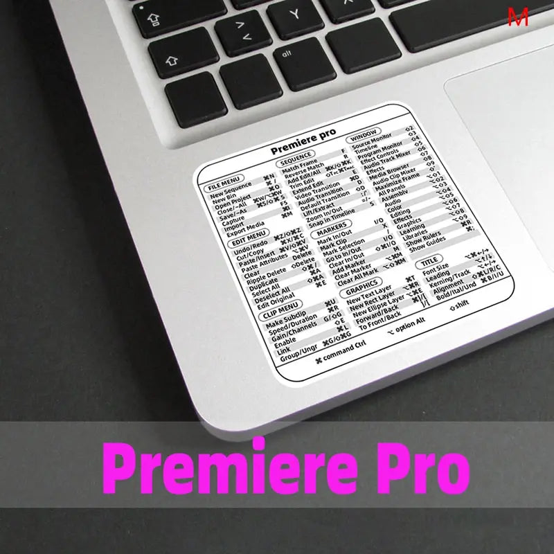A close-up of a laptop keyboard displaying the Premiere Pro shortcut quick reference sticker.