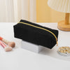 Black zippered pencil case resting on a white surface next to a makeup brush and a wooden lamp base.