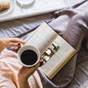 A person holds a cup of coffee while reading a book with decorative Bible verse bookmarks on the page.