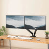 A dual monitor setup featuring two screens displaying a misty landscape, mounted on an ergonomic black adjustable arm.