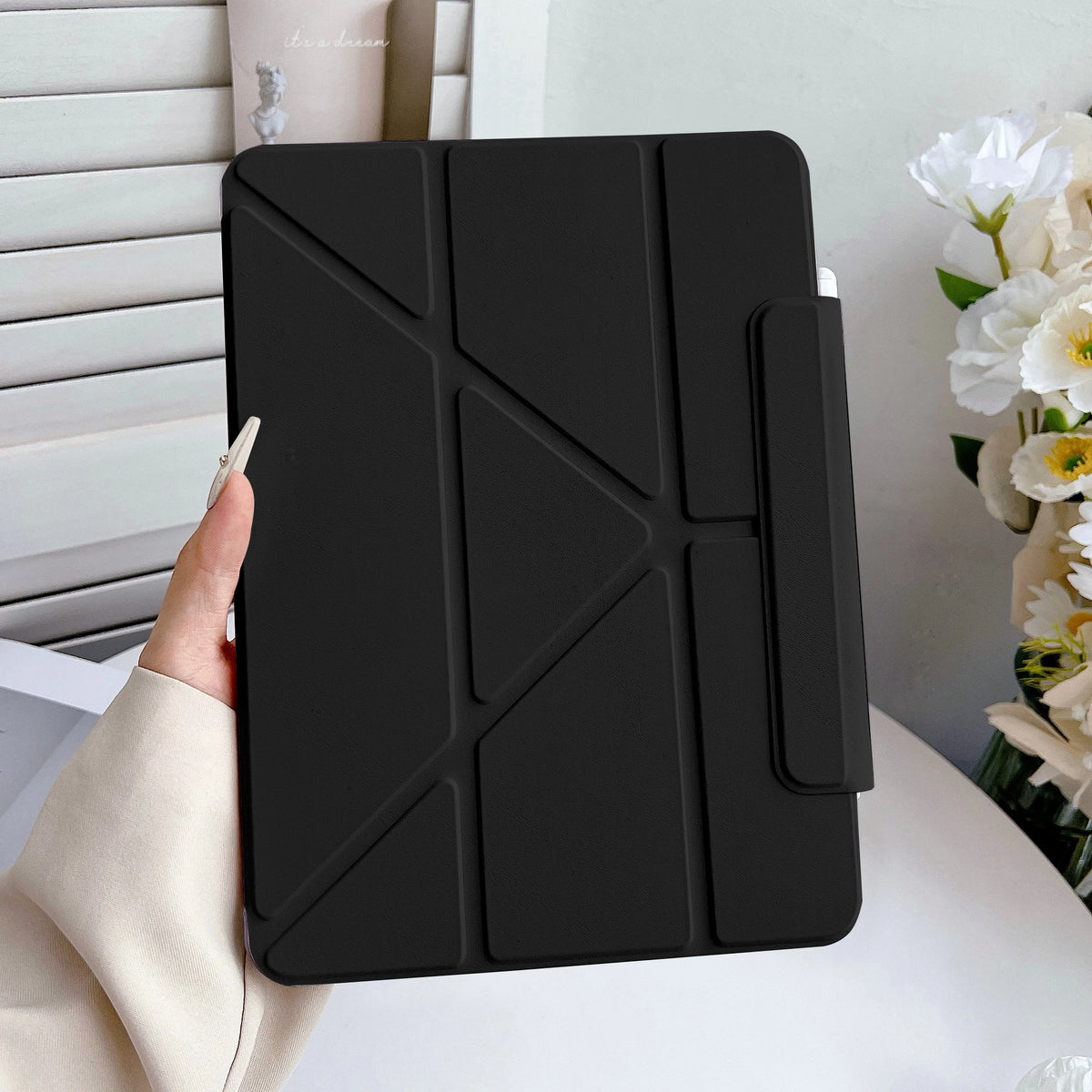 Estuche protector de cuero falso negro para iPad, sostenido por una mano contra fondo blanco.