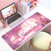 A large pink and purple The Sims gaming mouse pad with stitched edges is displayed next to a laptop and stationery.