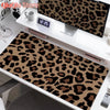 A large leopard print desk pad is displayed on a white desk next to a digital clock and other accessories.