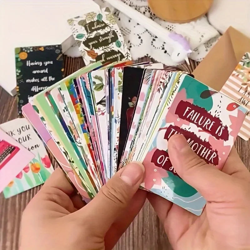 A hand holds a stack of colorful motivational greeting cards featuring nature and inspirational quotes.