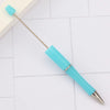 A light blue DIY beadable pen with a metal tip and a plastic cap resting on a white surface.