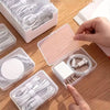 A hand is arranging white cables and connectors inside an open plastic storage box on a wooden desk.