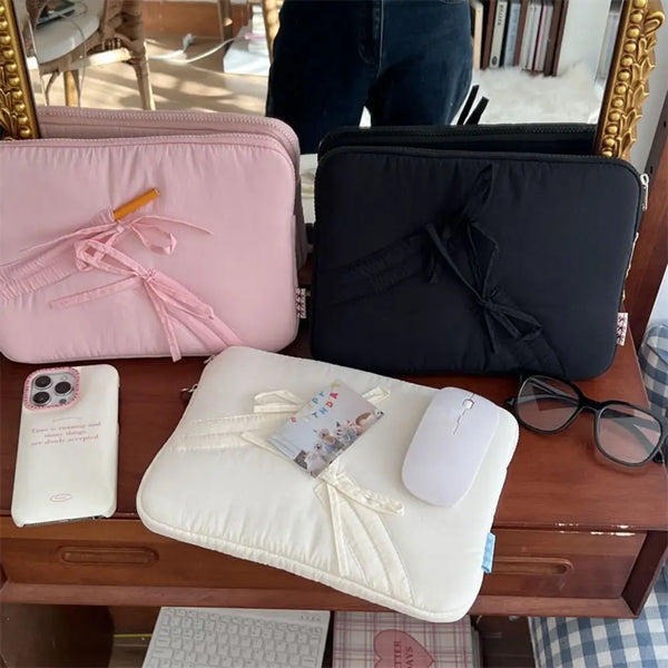A collection of pink and black laptop sleeves, including a white padded sleeve with a mouse, resting on a wooden surface.
