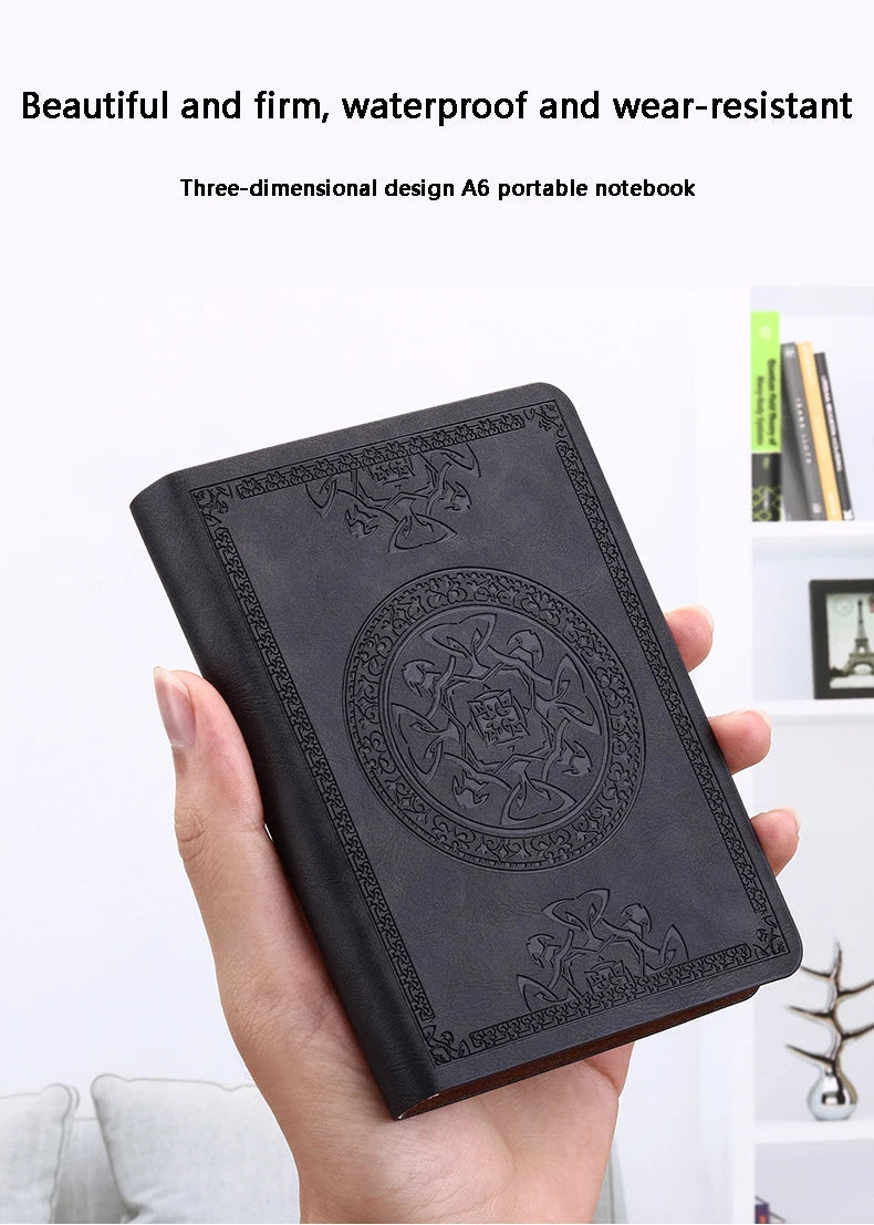A hand holds a black retro PU leather pocket notebook with an embossed design.