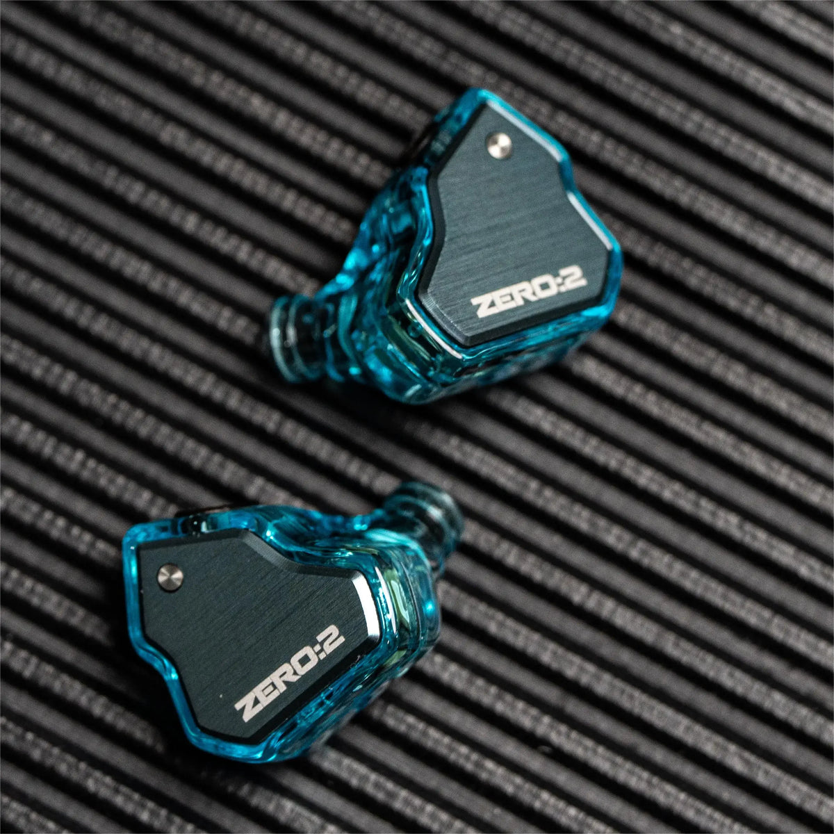 A pair of blue transparent in-ear monitors with a black housing and ZERO:2 branding resting on a dark textured surface.