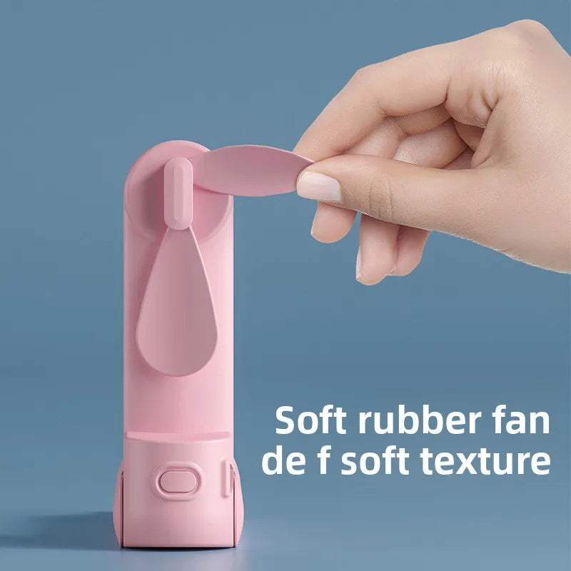 A hand holds a pink portable foldable rabbit mini fan with soft rubber texture against a blue background.