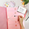 A pink expanding accordion document organizer file folder with thank you notes and a hand inserting a paper clip.