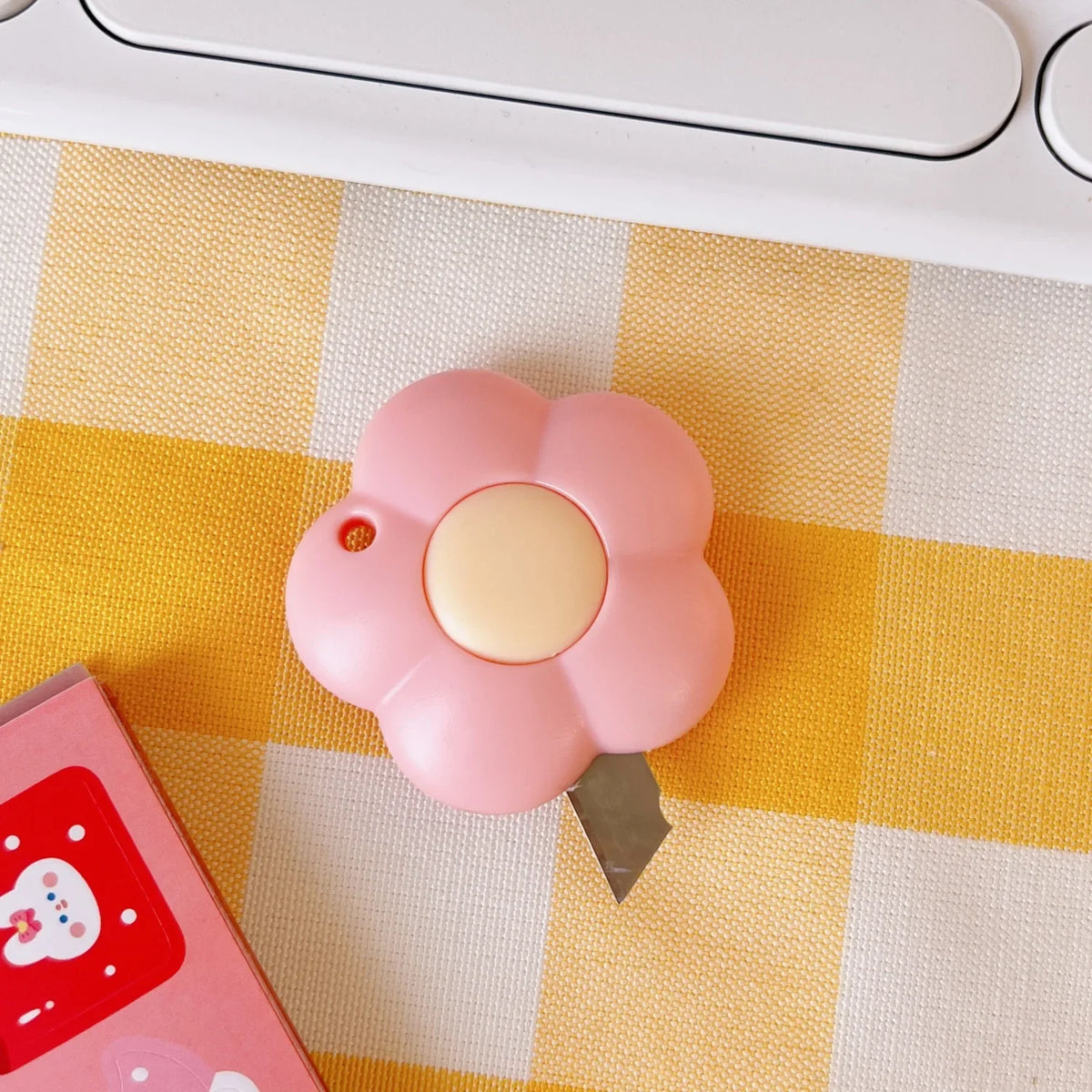 A pink cat paw mini cutter is shown resting on a yellow and white checkered surface.