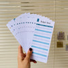 A hand holds a stack of A6 budget sheets with envelope pockets and expense tracking for financial planning.