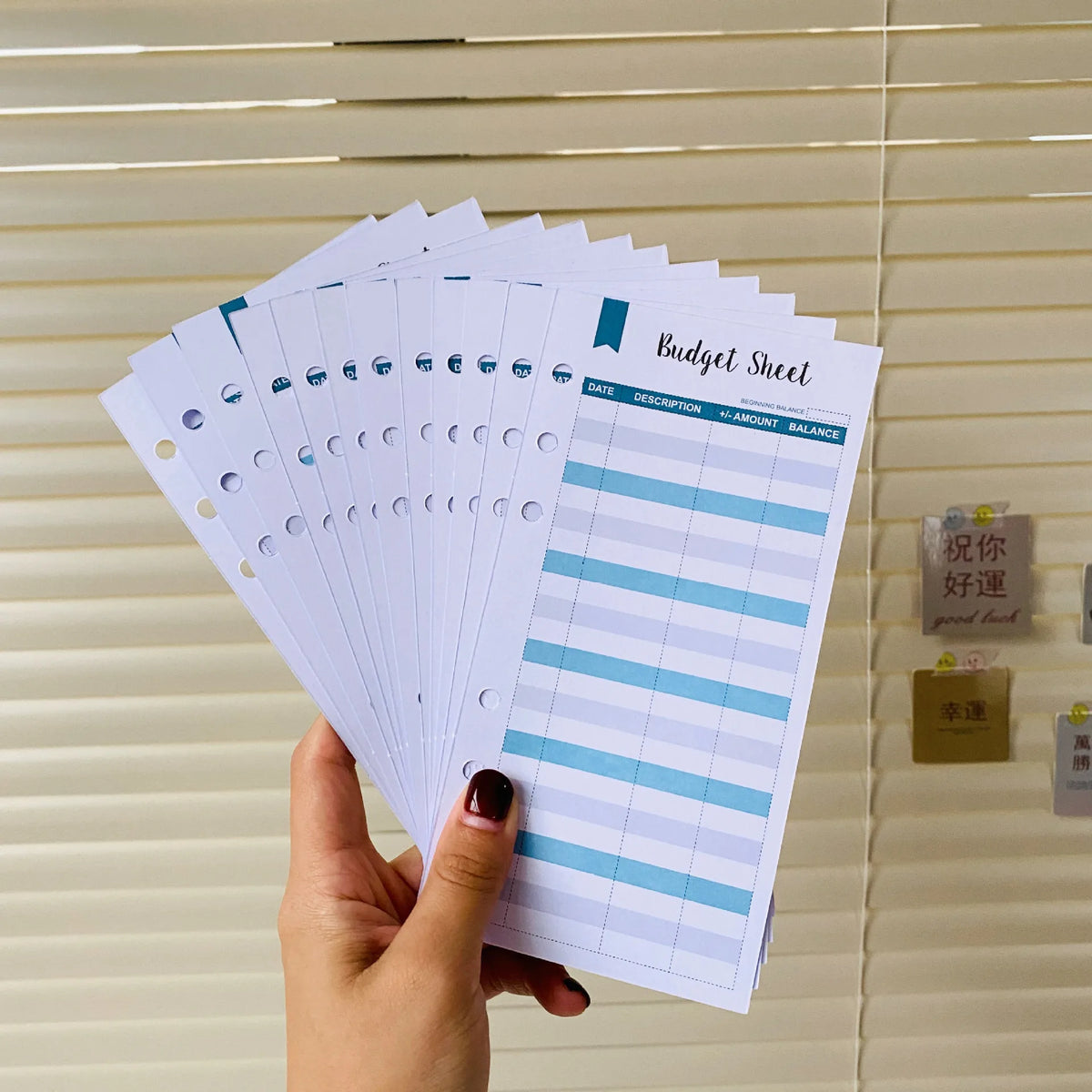 A hand holds a stack of A6 budget sheets with envelope pockets and expense tracking for financial planning.