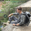 A man uses a built-in compass and carabiner for navigation while outdoors with a solar power bank.