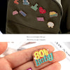 A set of enamel pins featuring 80s baby designs and a heart-shaped pin on a hand.