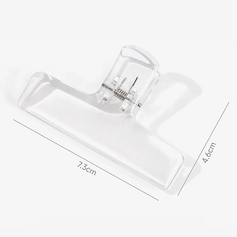 A clear plastic book page clip with a tapered shape shown against a white background.