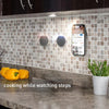 A magnetic phone mount is attached to a kitchen backsplash, showing a smartphone displaying a video.