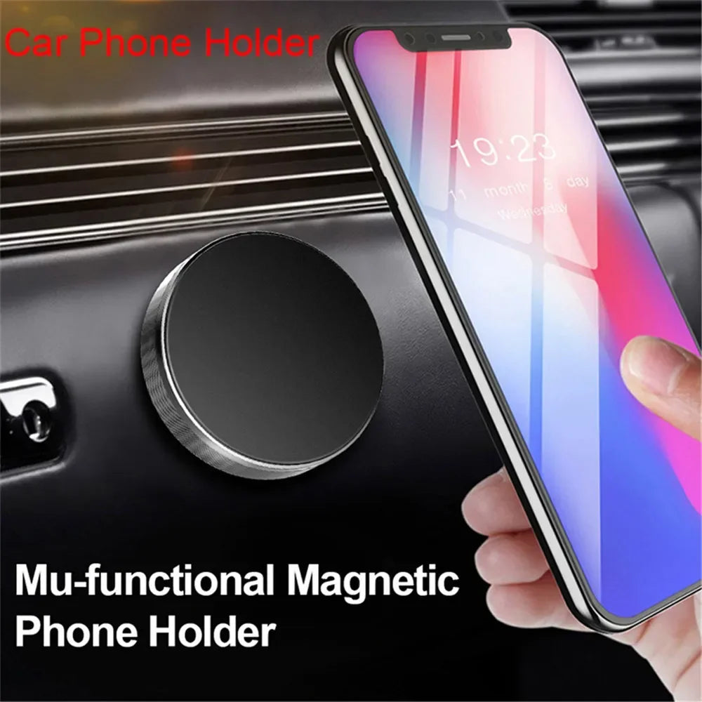 A hand holds a smartphone attached to a magnetic car dashboard phone holder.