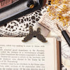 A vintage butterfly metal book clip resting on aged paper and a dark surface.