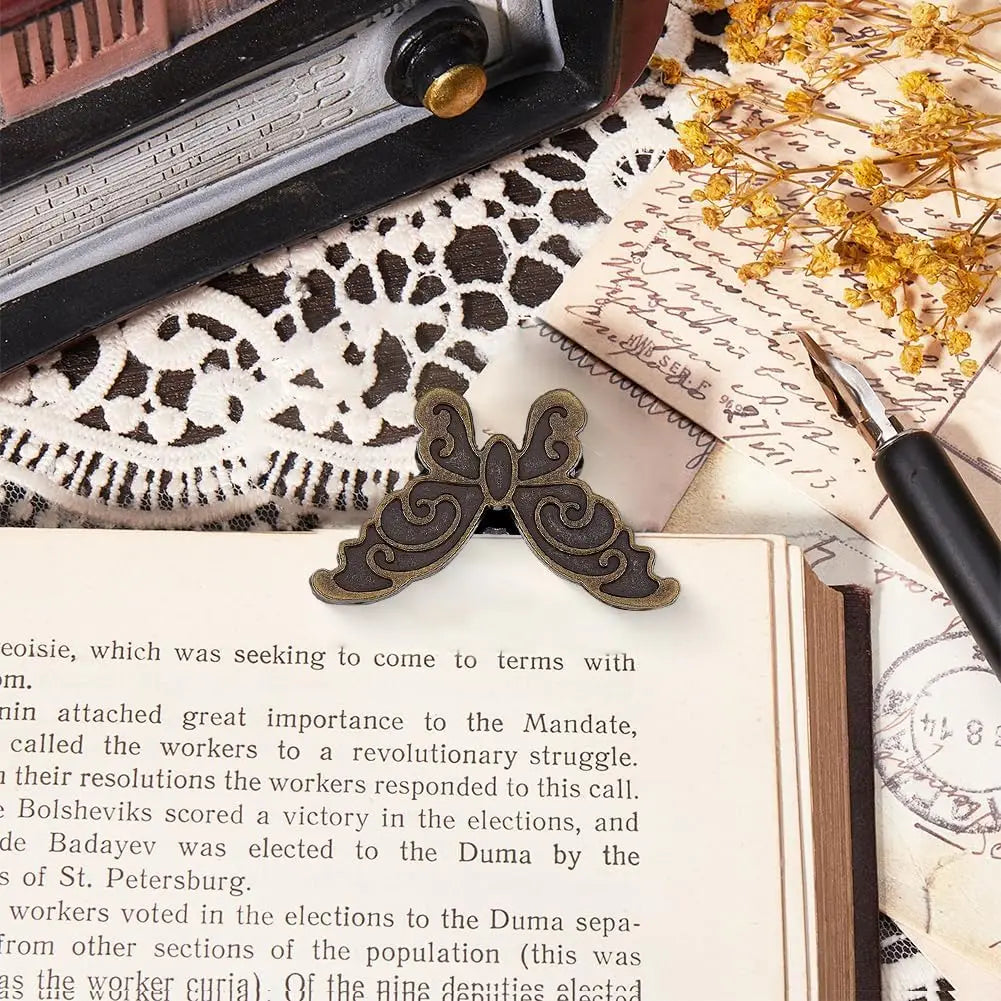 A vintage butterfly metal book clip resting on aged paper and a dark surface.