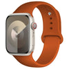 A silver Apple Watch is shown attached to an orange silicone sport band.