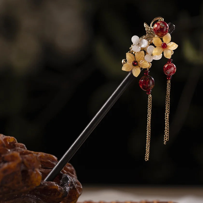 Accessoires pour cheveux dorés avec des fleurs en bois et des perles rouges sur un bâtonnet fin.
