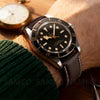 A close-up of a brown leather watch with quick release pins on a wrist, next to a vintage pocket watch.